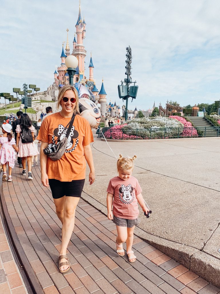 Woman and child walk in front of large pink and blue castle at Disneyland Paris