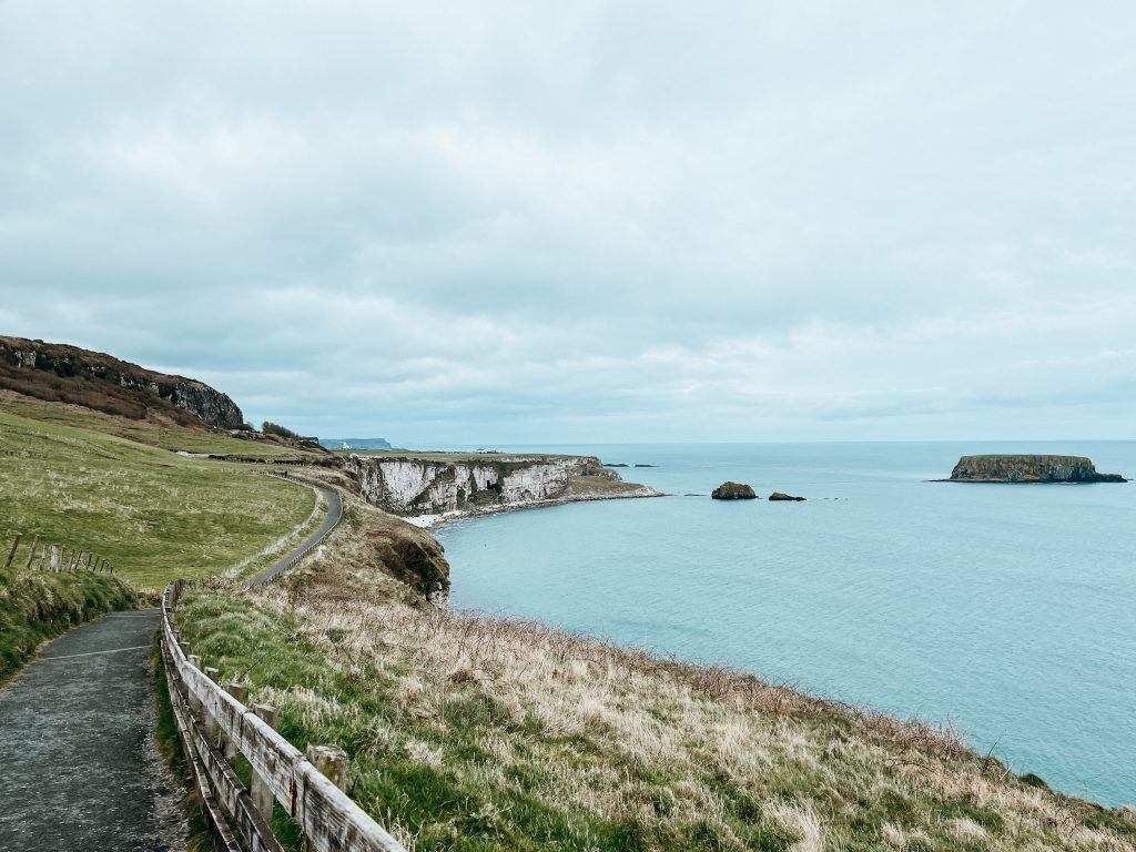 Trail along green and white cliffs next to bright blue water in Northern Ireland by the Carrick-A-Rede Rope Bridge