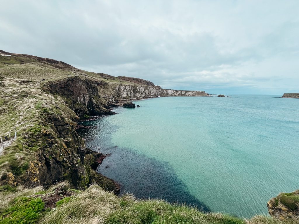 Views of green and white cliffs along bright blue water in Northern Ireland by the Carrick-A-Rede Rope Bridge