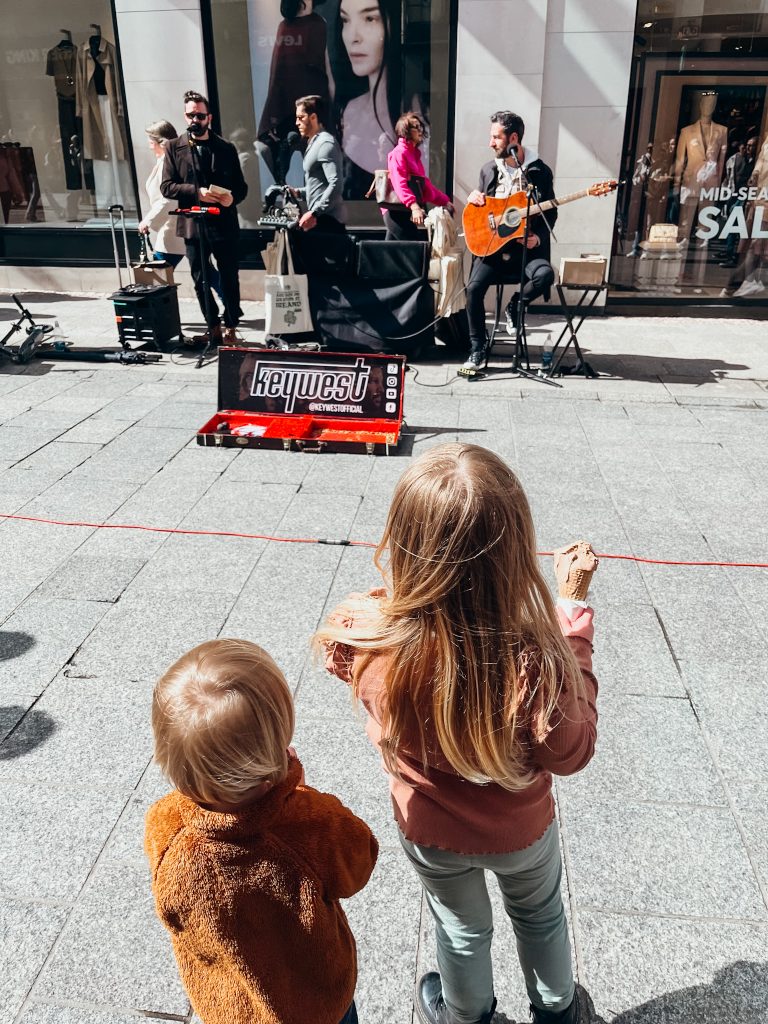 Two children watch musicians playing music on a pedestrian street in Dublin