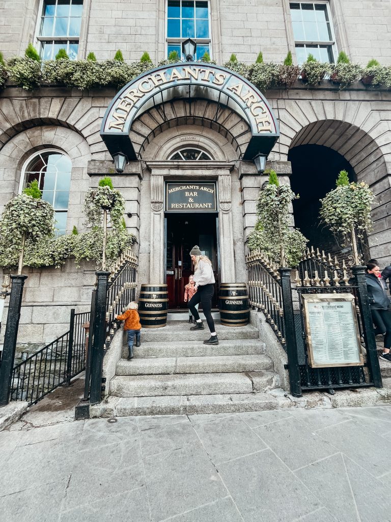 Woman and two children climb the steps up to a grey colored building with a sign that reads Merchant's Arch Bar