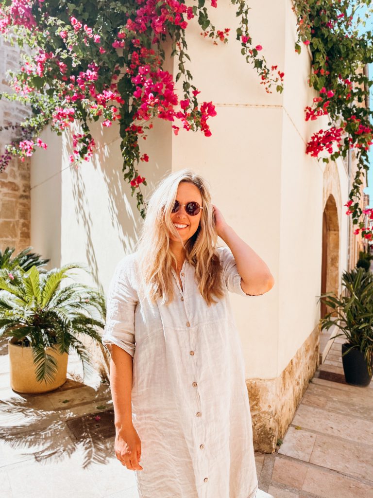 Woman wearing sunglasses stands in front of a white building covered in pink flowers