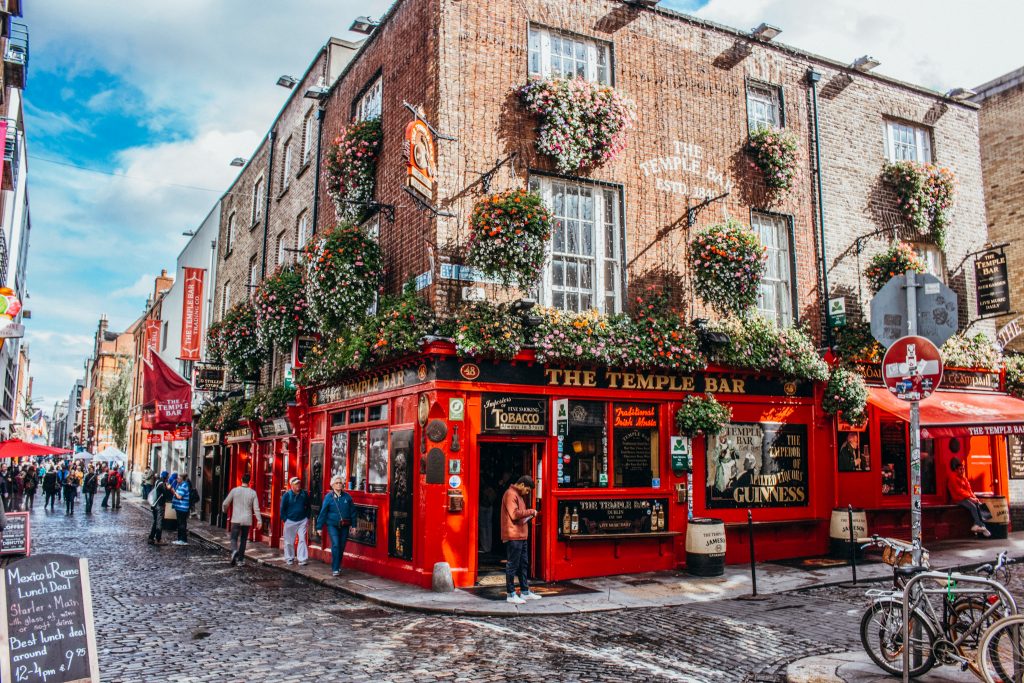 Bright right building on a corner covered in flowers with a sign that reads ' The Temple Bar'