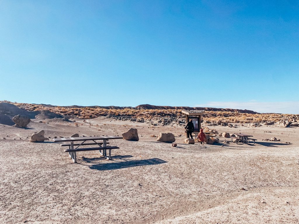 Large area of dirt with three picnic tables and a large sign