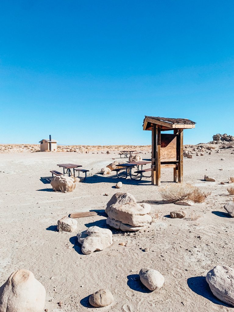 Large rocks and three picnic tables with a big wooden sign in a large area of dirt