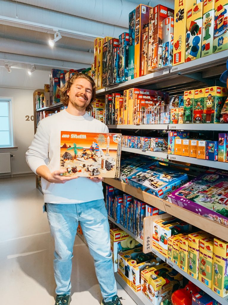 Man stands holding a LEGO box next to shelves full of LEGO boxes