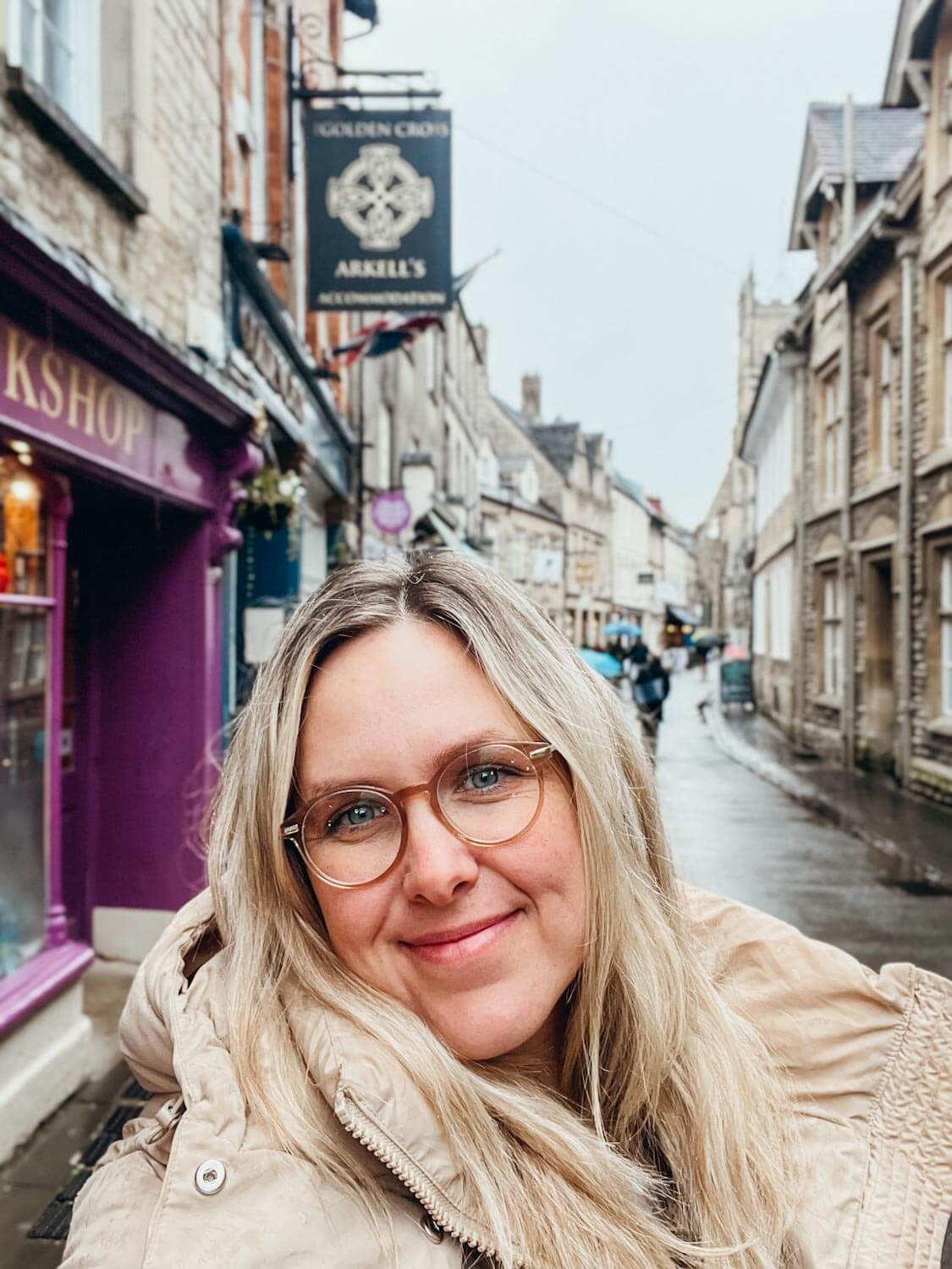 Woman stands on sidewalk with a curved road lined with old brick buildings in Cirencester