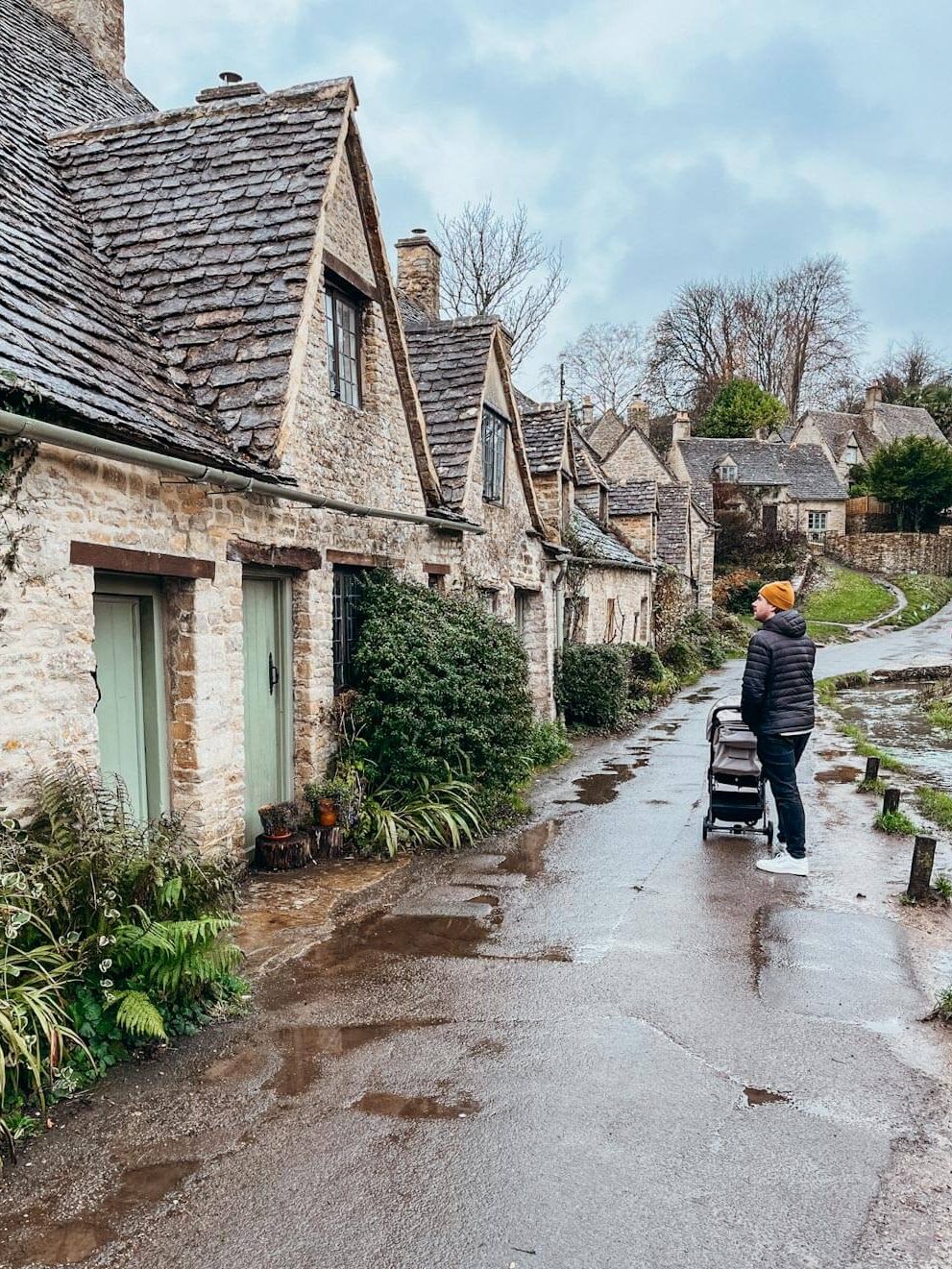 Man pushes stroller on wet paved road next to row of old brick buildings
