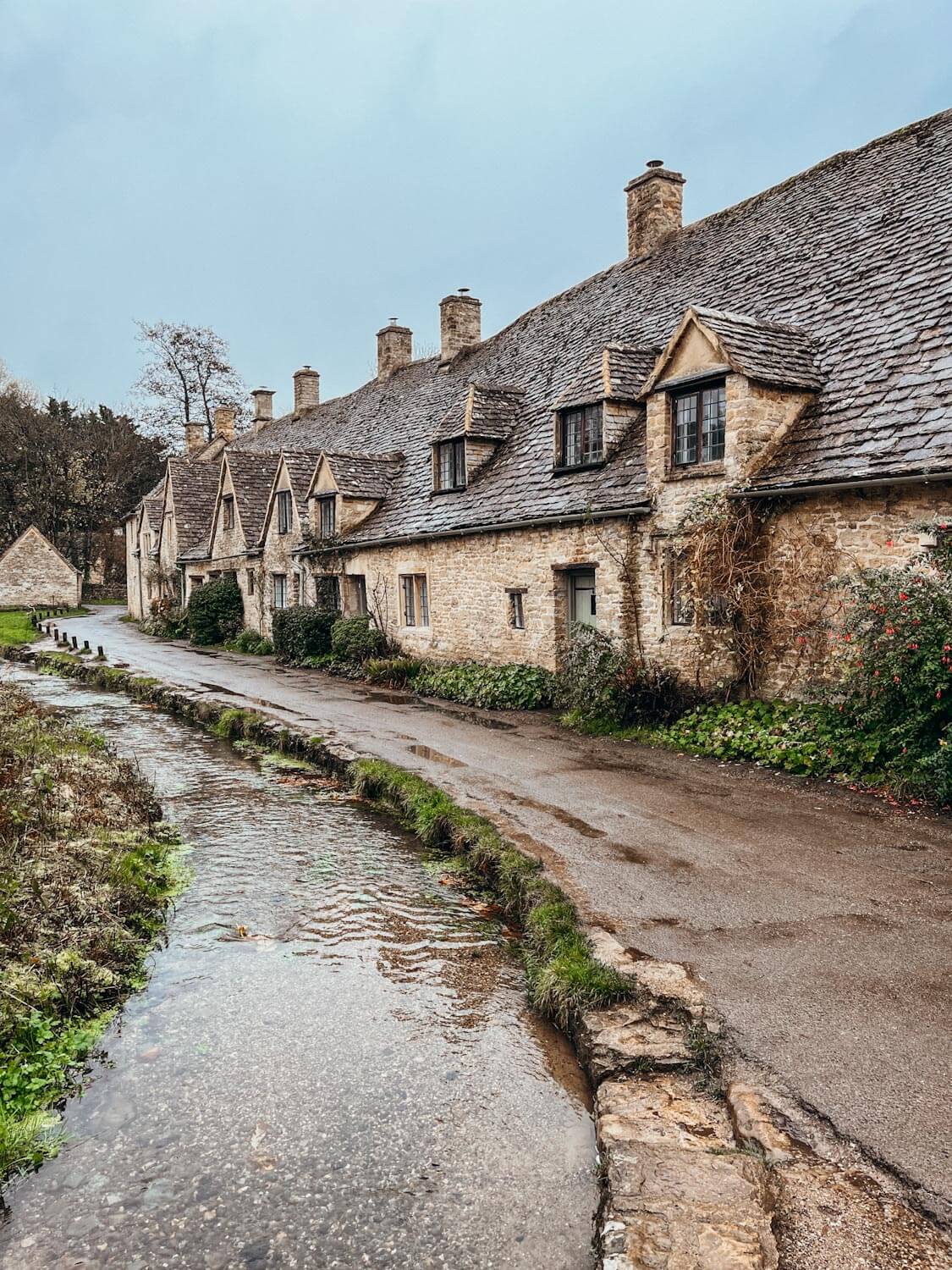 Row of old, honey-colored stone homes along a small stream in the Cotswolds