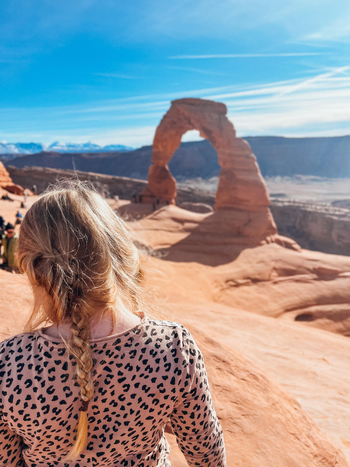 Girl stands in front of large red rock arch in Arches National Park in January