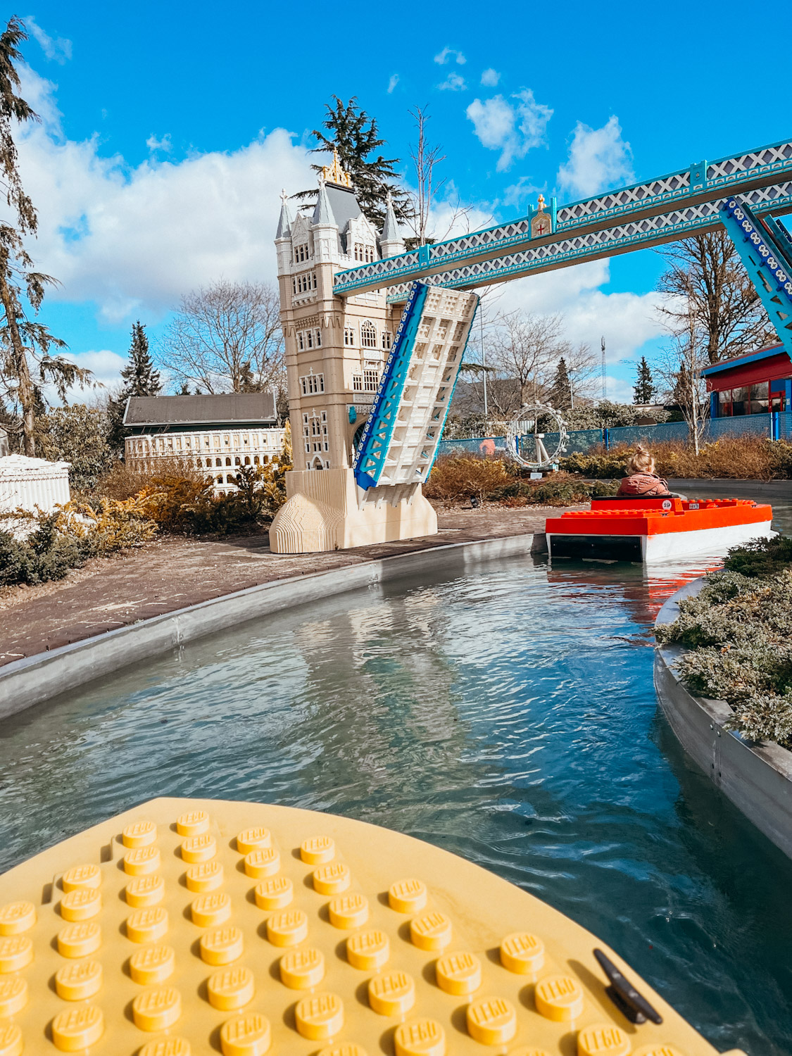 Small, yellow and red boats made of lego float down small stream at LEGOLAND in Denmark