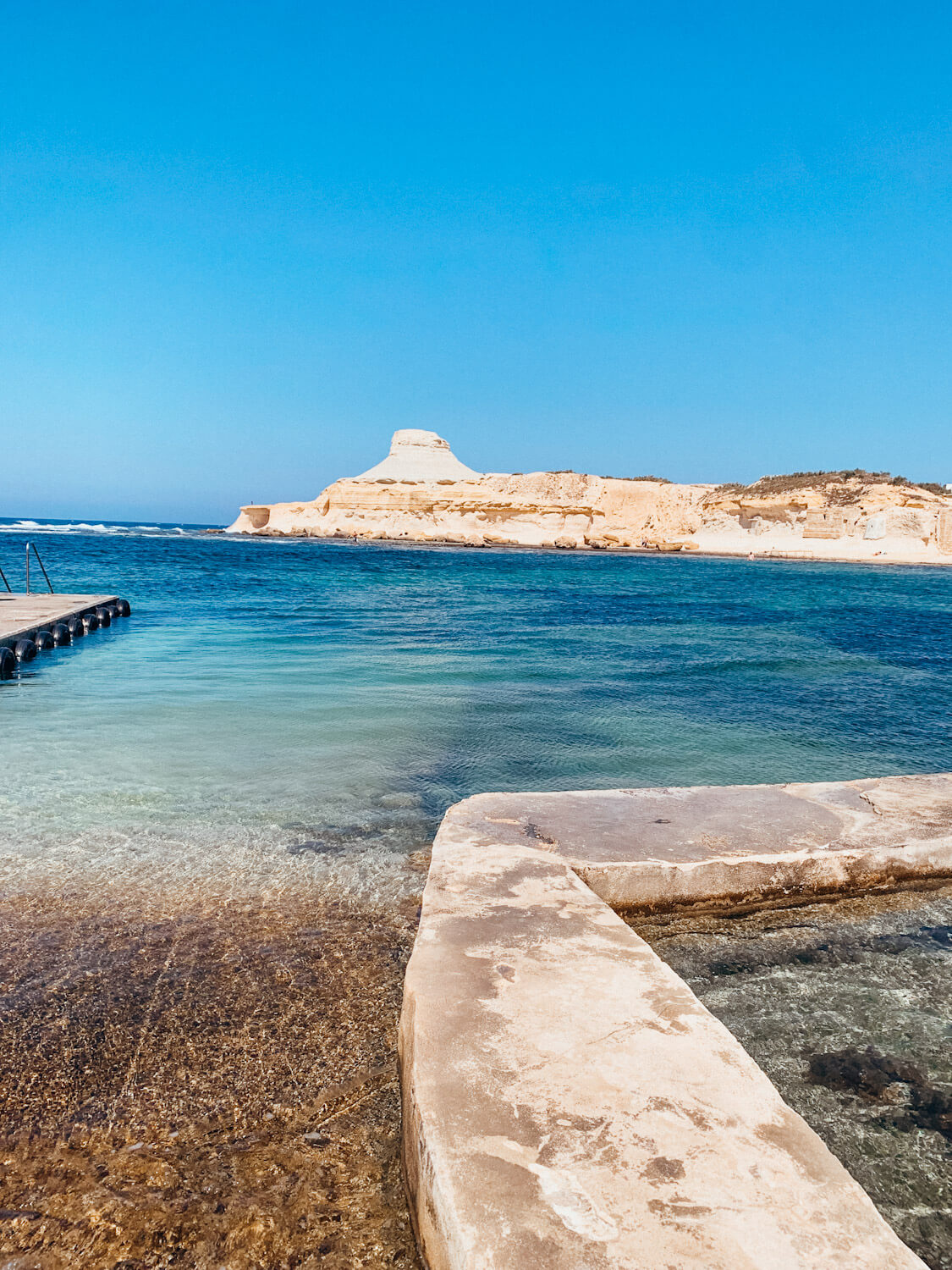 Cement dock leads into bright blue water with a white rock formation in the distance