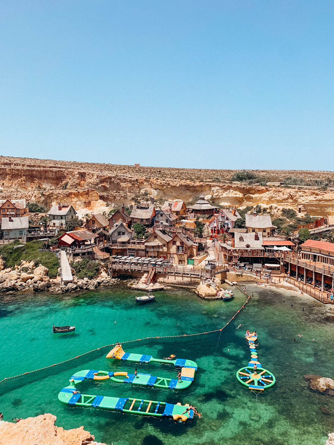 Ariel view of cove lined with wooden buildings and green water with colorful floating play spaces