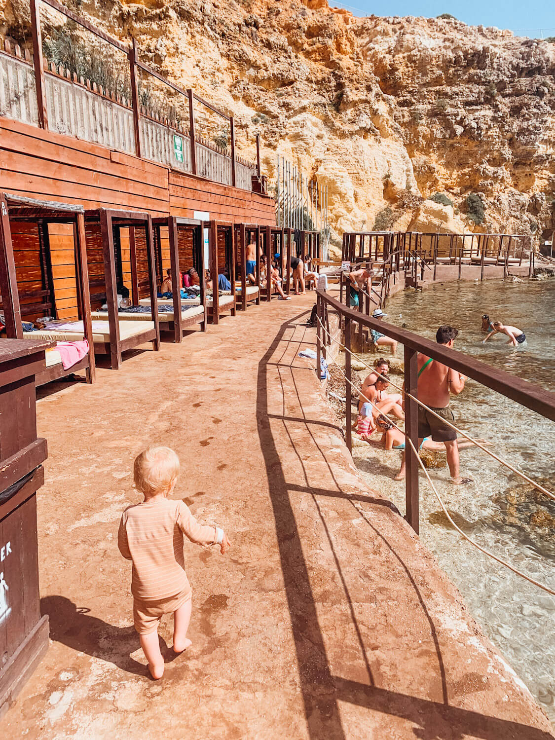 Child walks along cement path lined with sunbeds at Popey Village in Malta