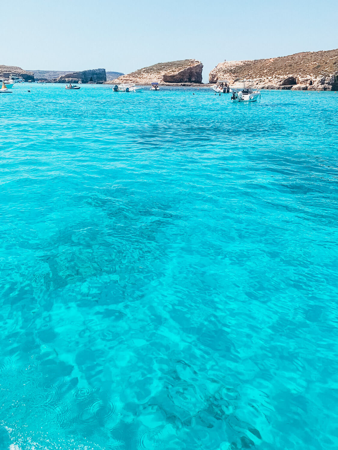 Bright blue water with white boats and a rocky island in the distance