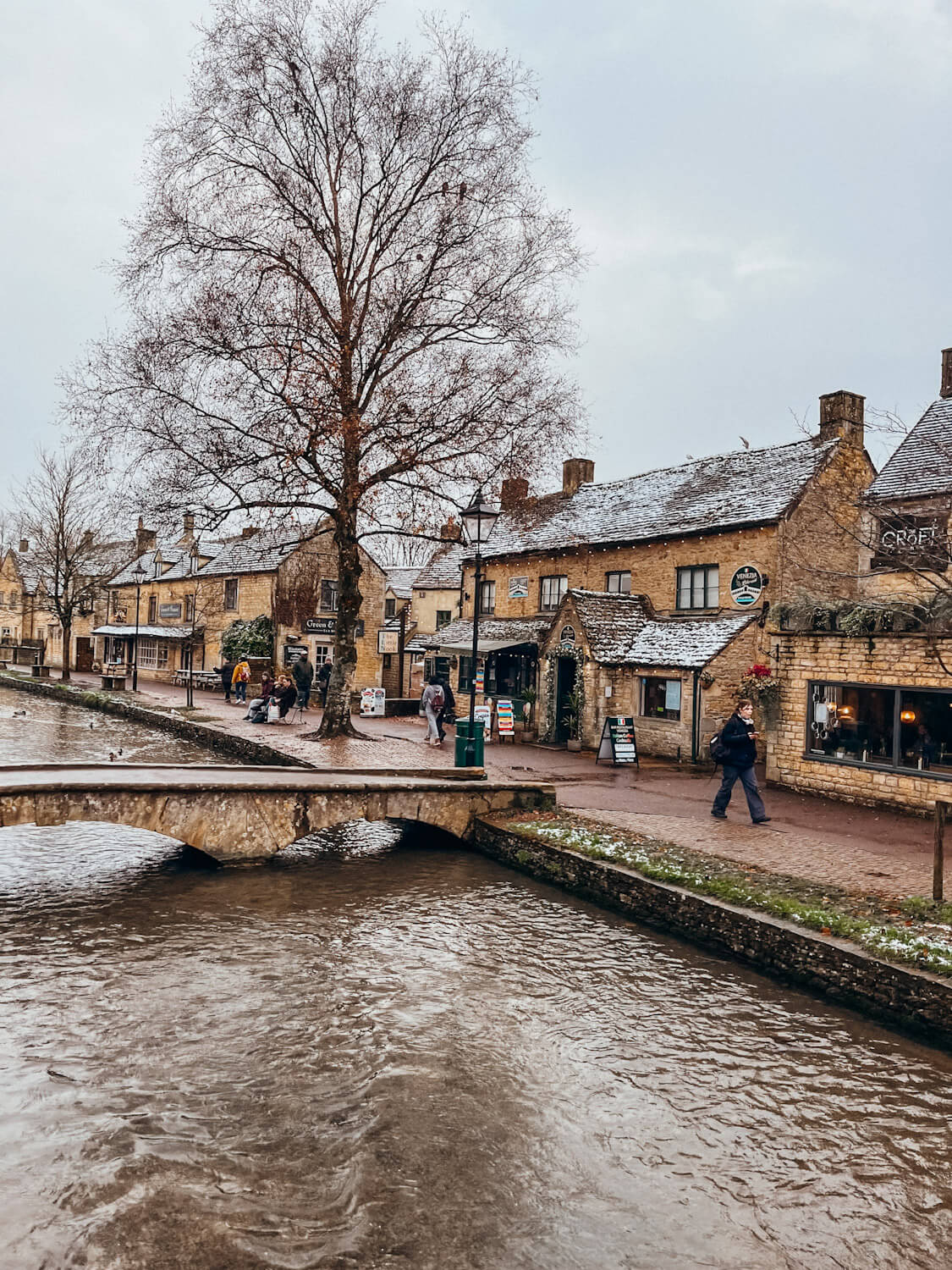 Stream runs along path of old stone shops in Bourton-on-the-Water in November