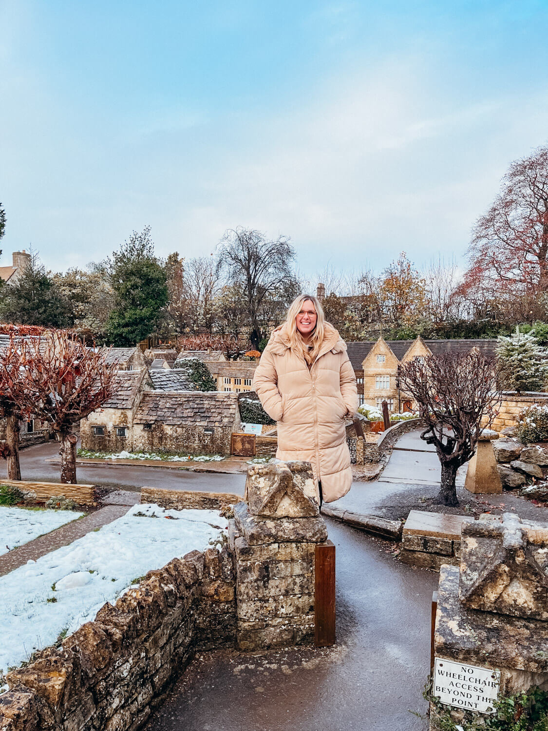 Woman stands amongst models of old stone buildings in the model village in Bourton-on-the-Water