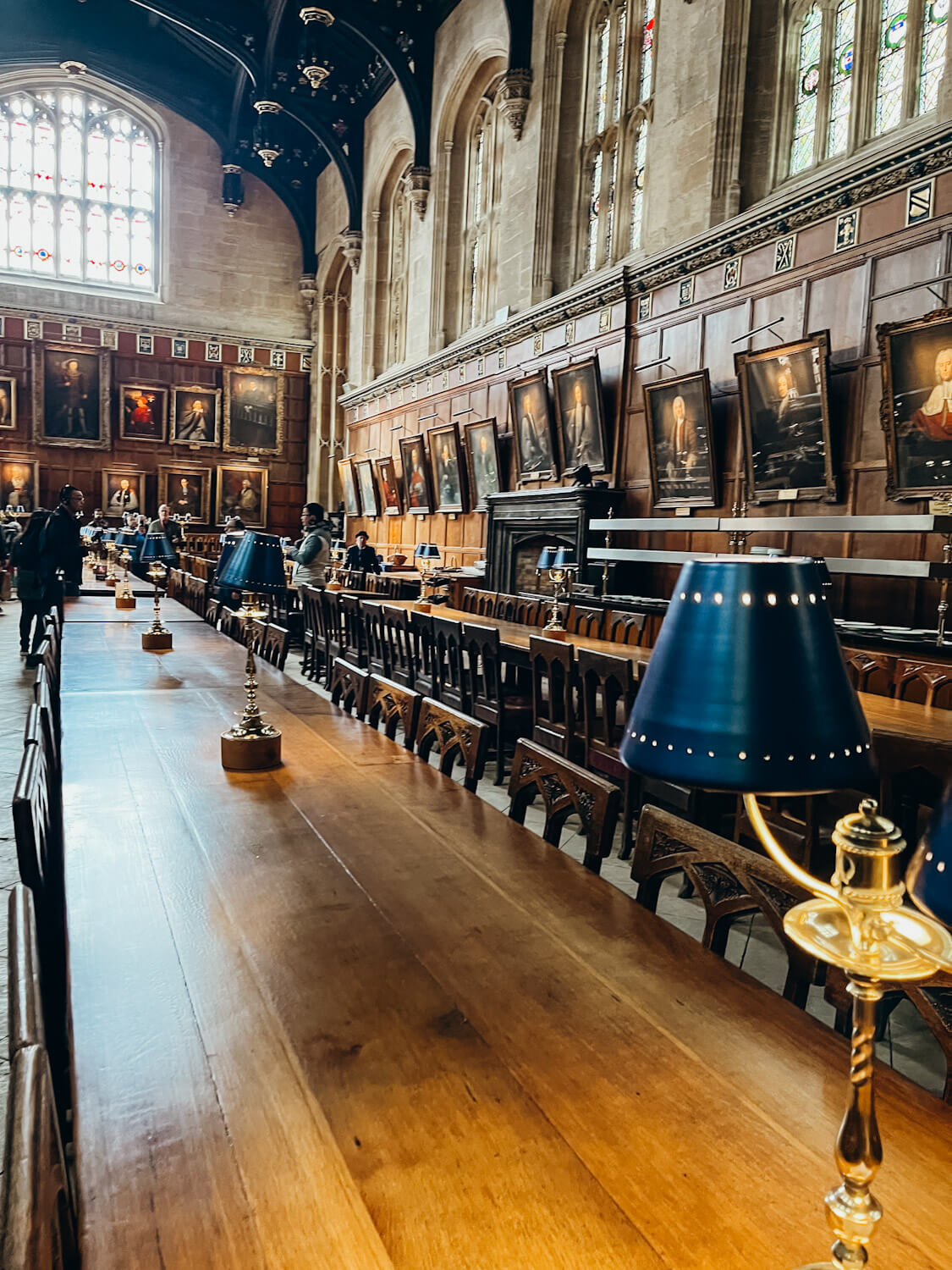 Wooden tables with blue lamps atop in grand dining hall at Christ Church College in Oxford