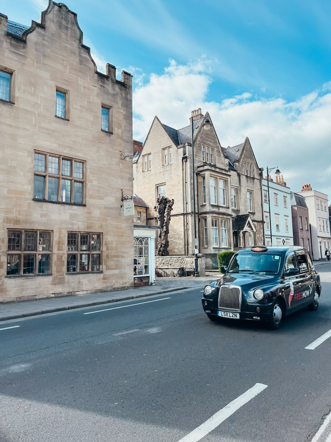 Black London taxi drives down road past old stone buildings in Oxford