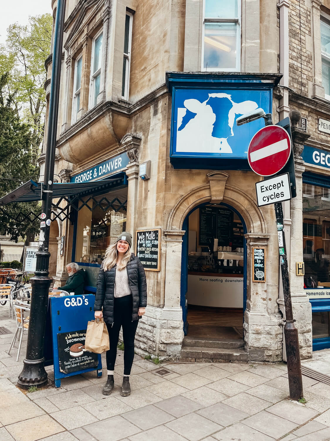Woman stands in front of stone storefront with blue signs attached