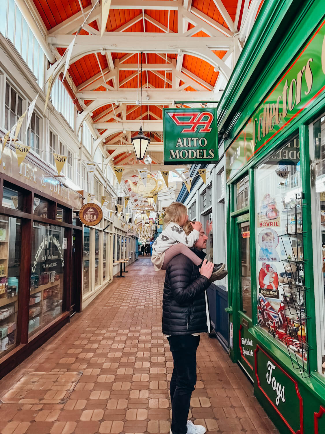 Man stands with child on his shoulders in front of store with green, wooden storefront in Oxford