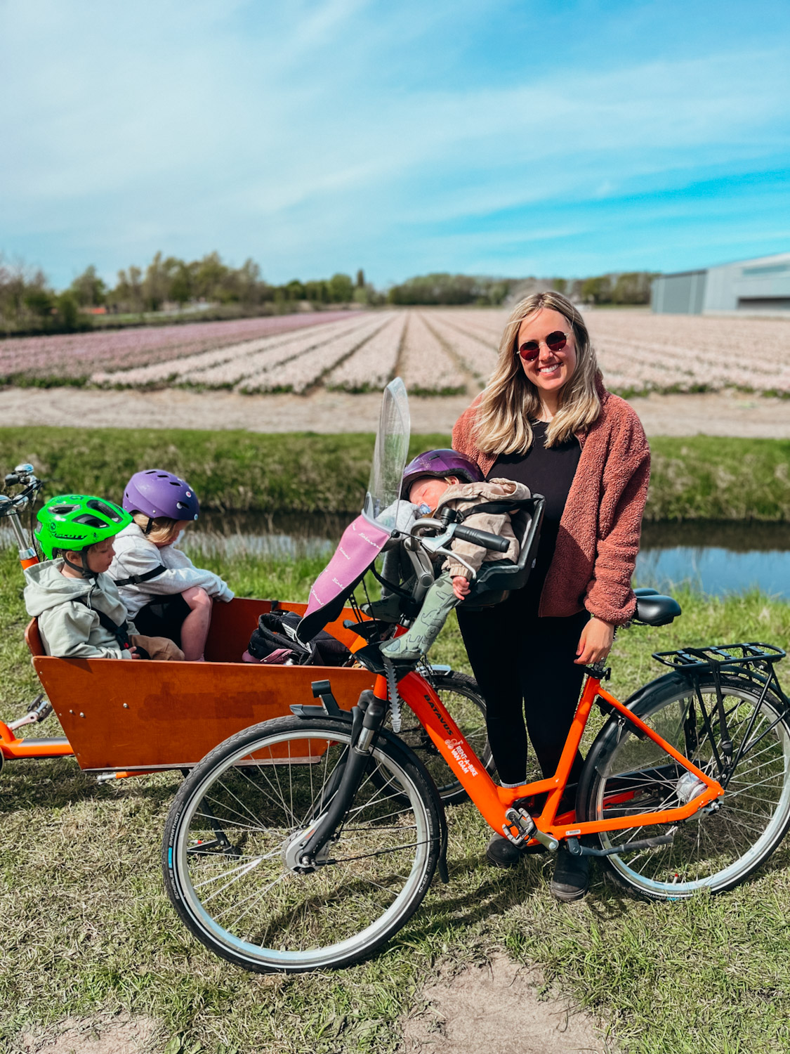 Mother and children sit on bikes in front of white and purple flower fields