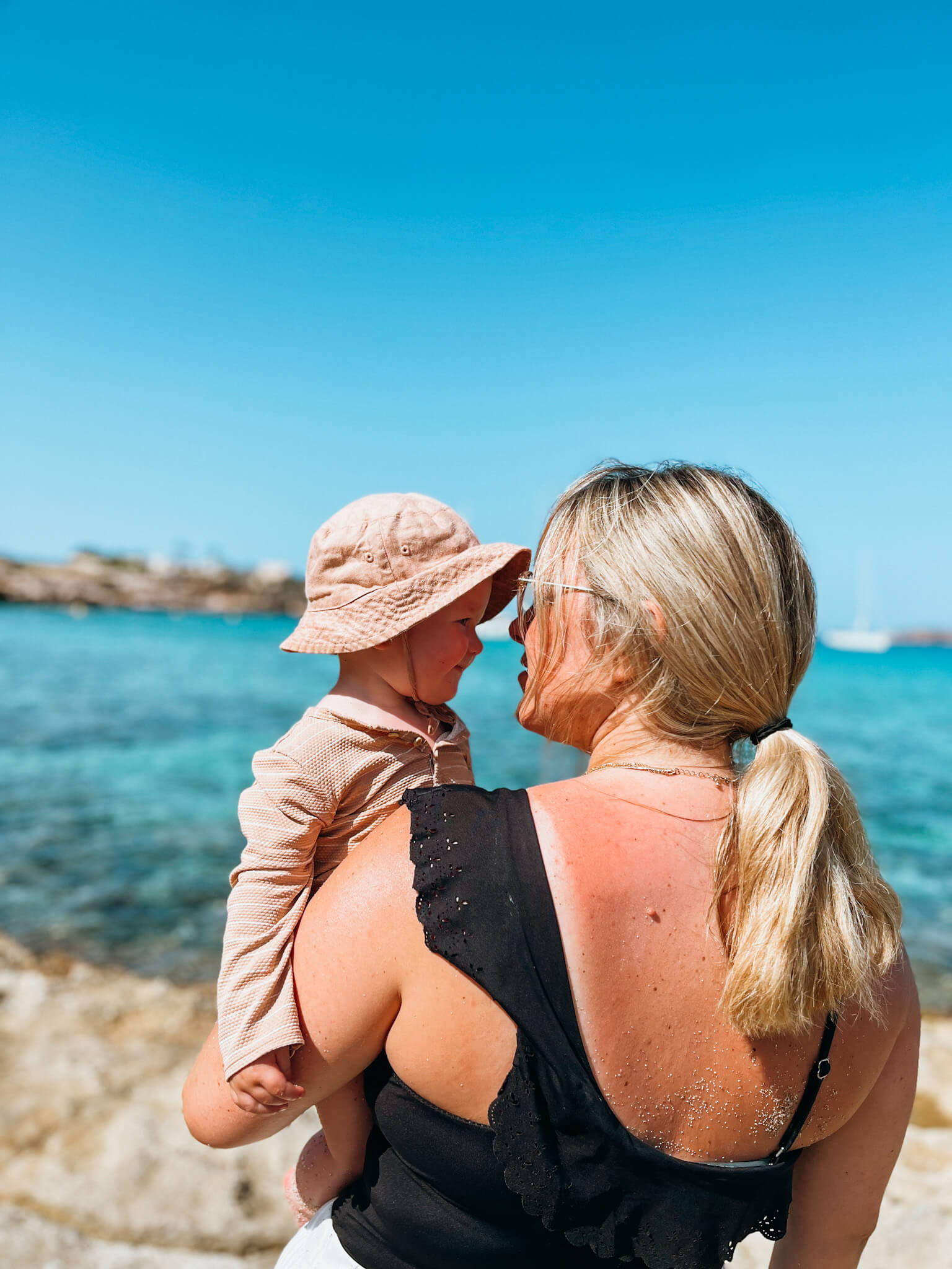 Woman and baby look at each other with blue water in the background