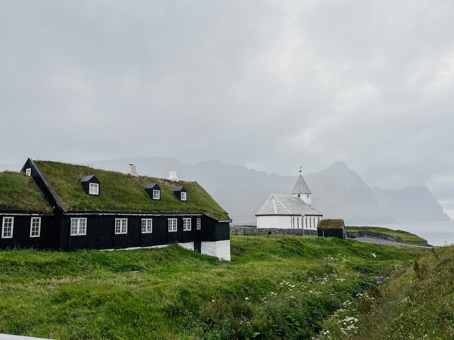 Grass covered building and old white church with views of mountains in the fog in the distance