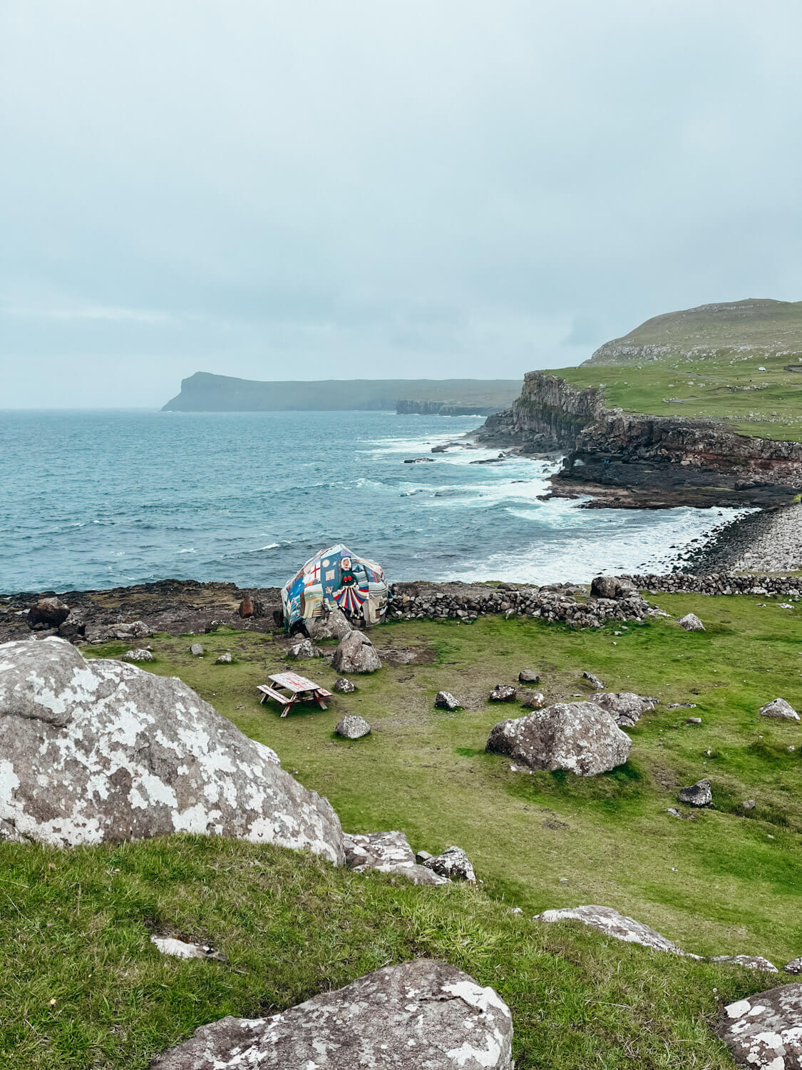 A large boulder covered with crocheted fabric next to the sea