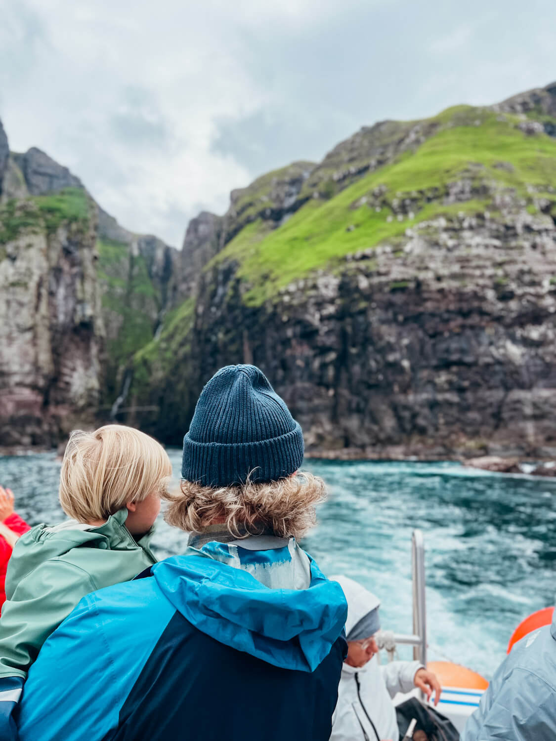 Man and child look out from boat and sea cliffs in the Faroes