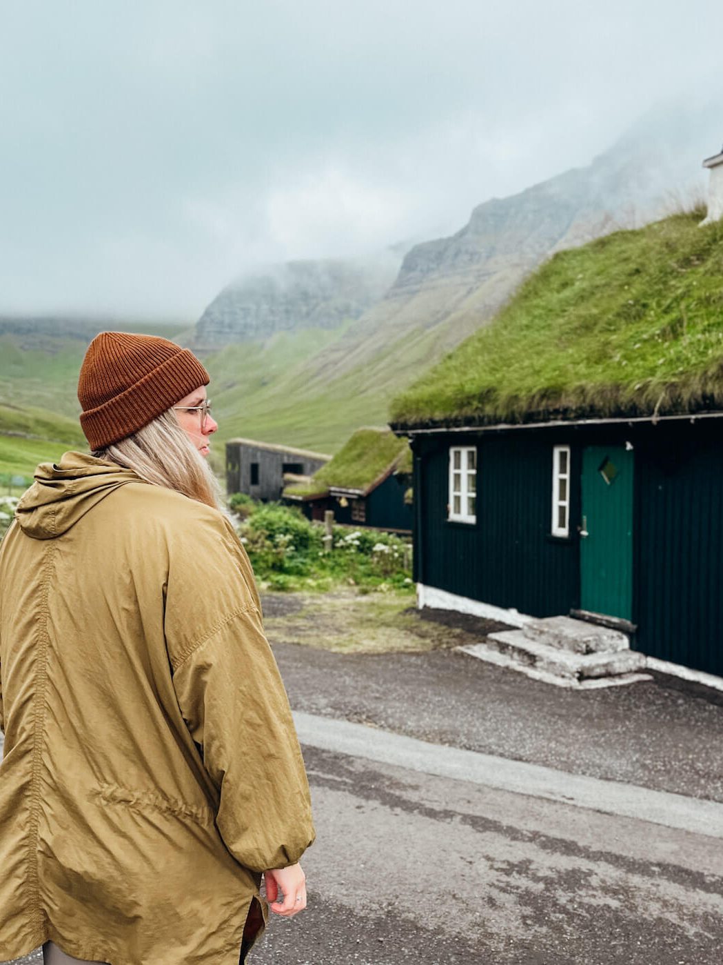 Woman stands in front of grass covered cottage in the Faroe Islands