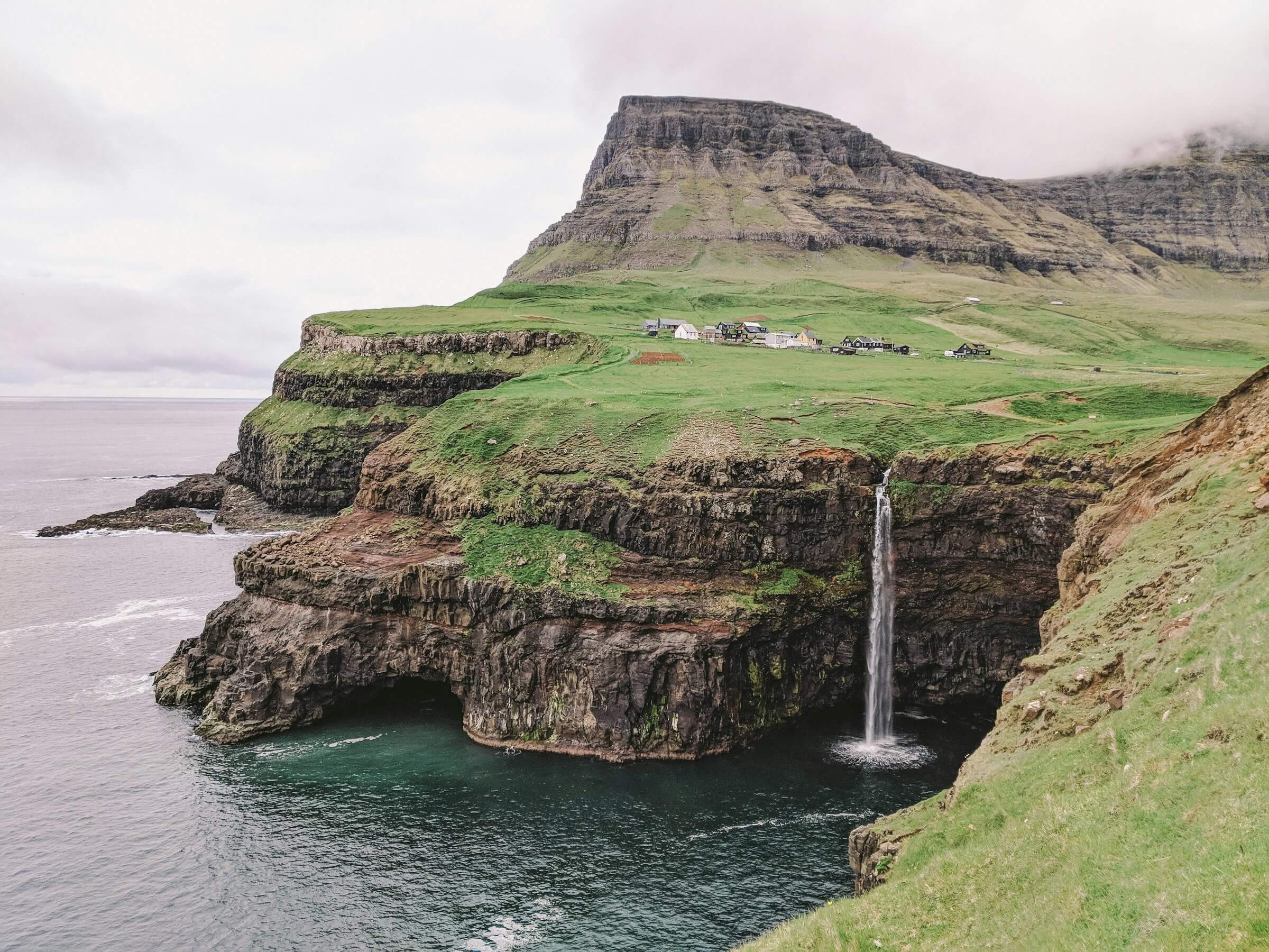 Waterfall falls from a green cliff into the ocean in the Faroe Islands