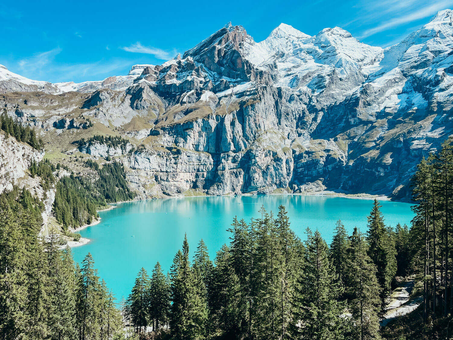 Bright turquoise blue lake surrounded by pine treese and snow-capped mountains : Lake Oeschinensee Switzerland