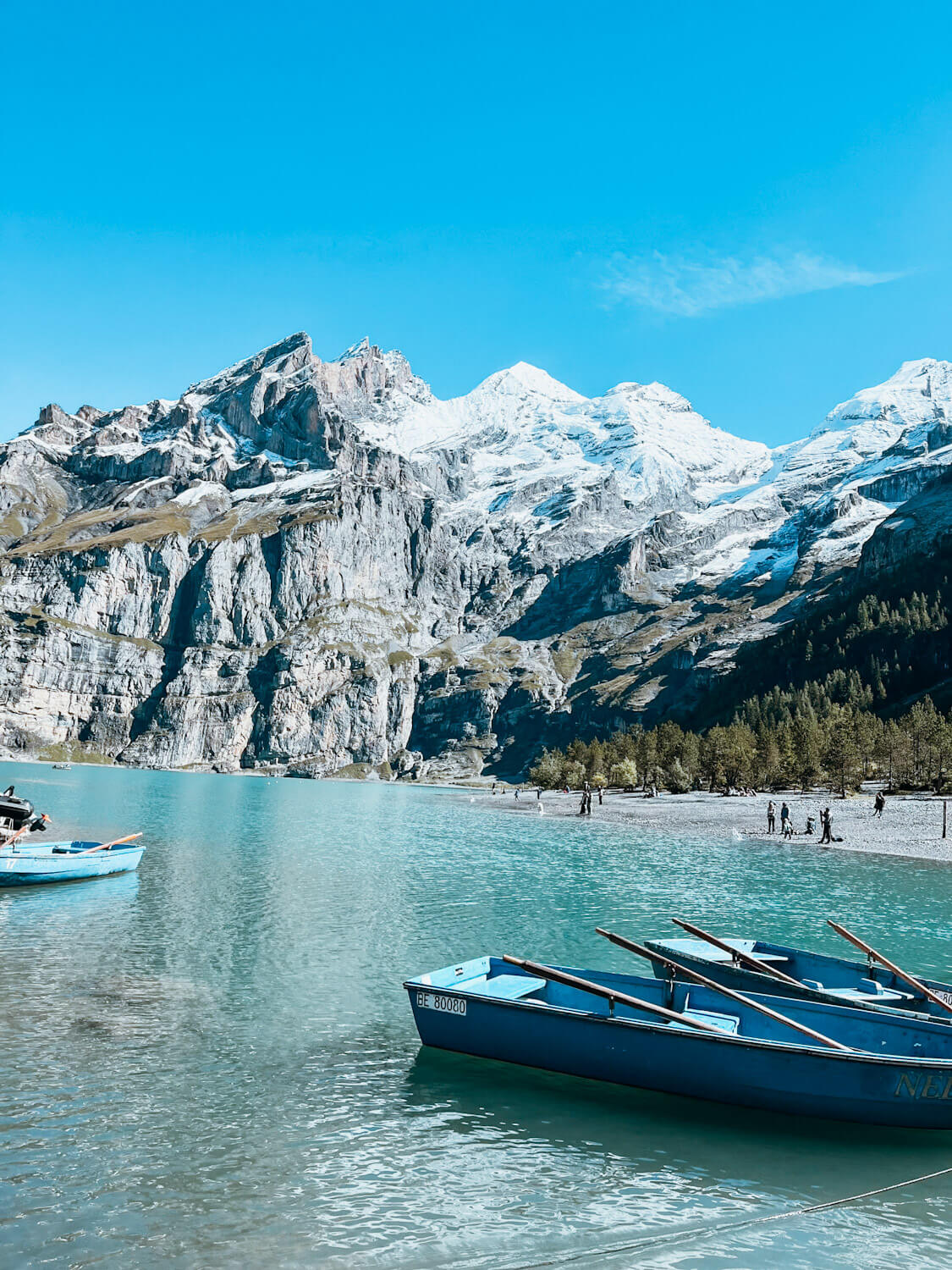 Bright turquoise blue lake with multiple blue rowbaots surrounded by snow-capped mountains : Lake Oeschinensee Switzerland