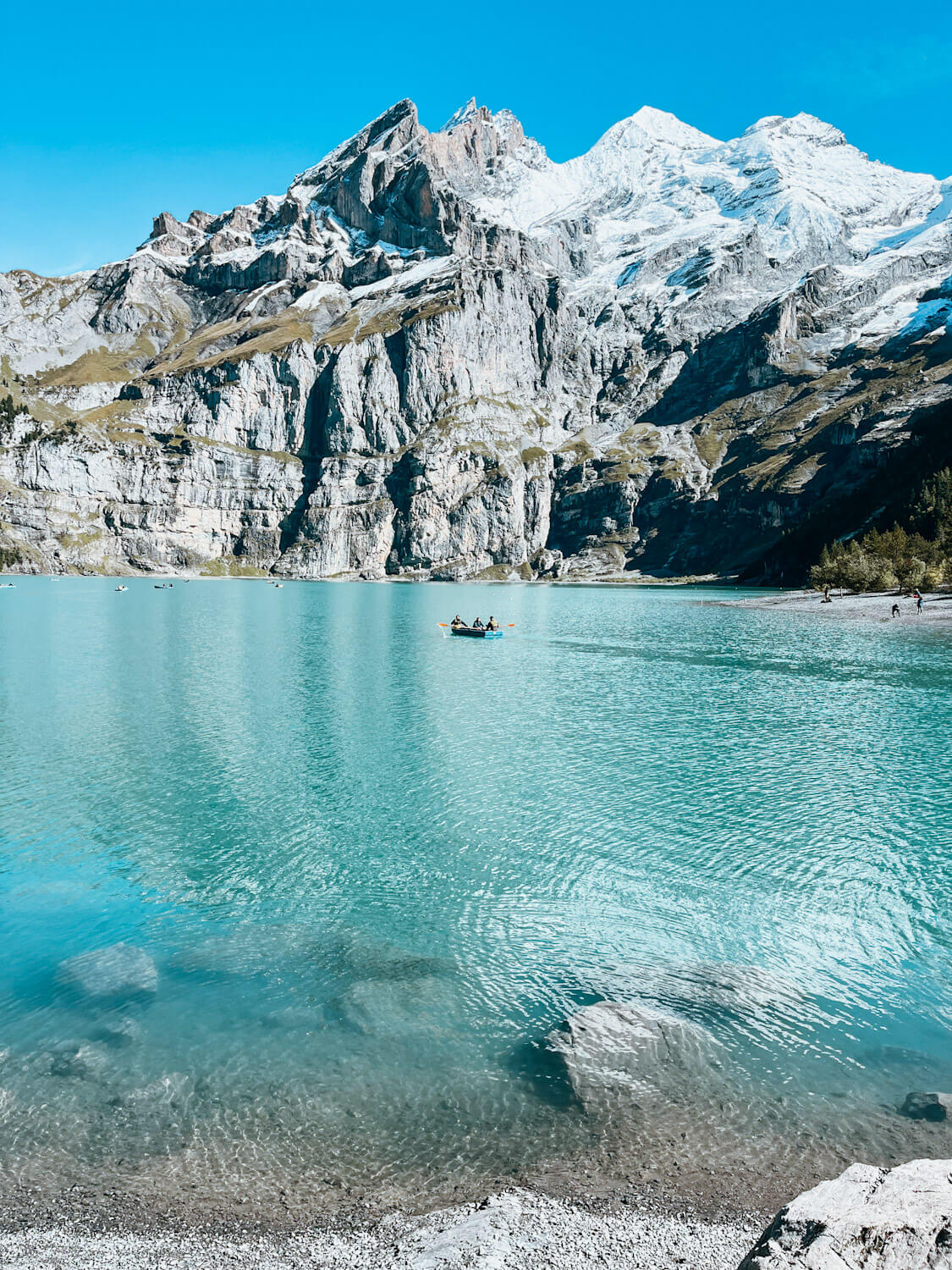 Bright turquoise blue lake with one rowboat on it surrounded by snow-capped mountains : Lake Oeschinensee Switzerland