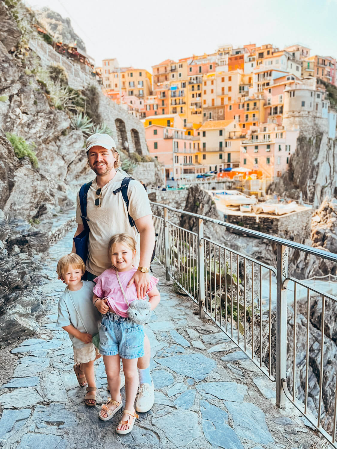 Father and two children stand in paved walkway with colorful village behind them