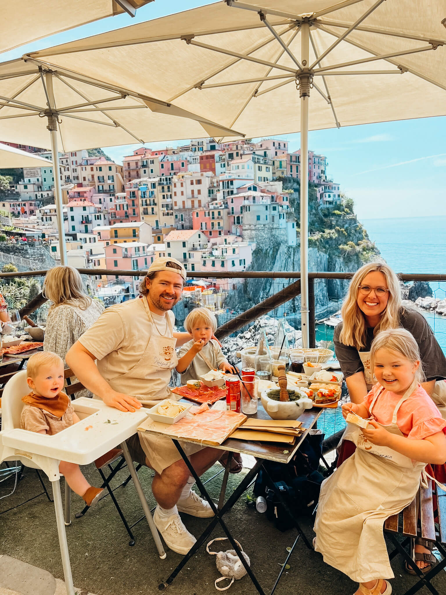 Young family sits at lunch table at Nessun Dorma restaurant with colorful village views behind them