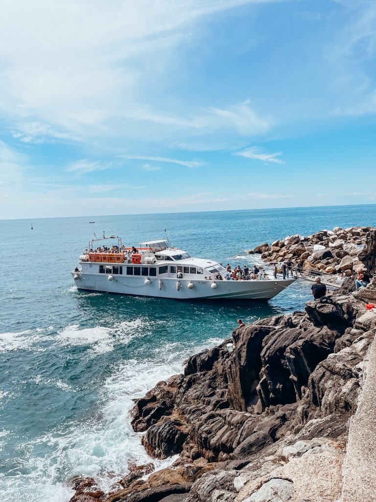 Large white boat docking next rocks in Riomaggiore Cinque Terre
