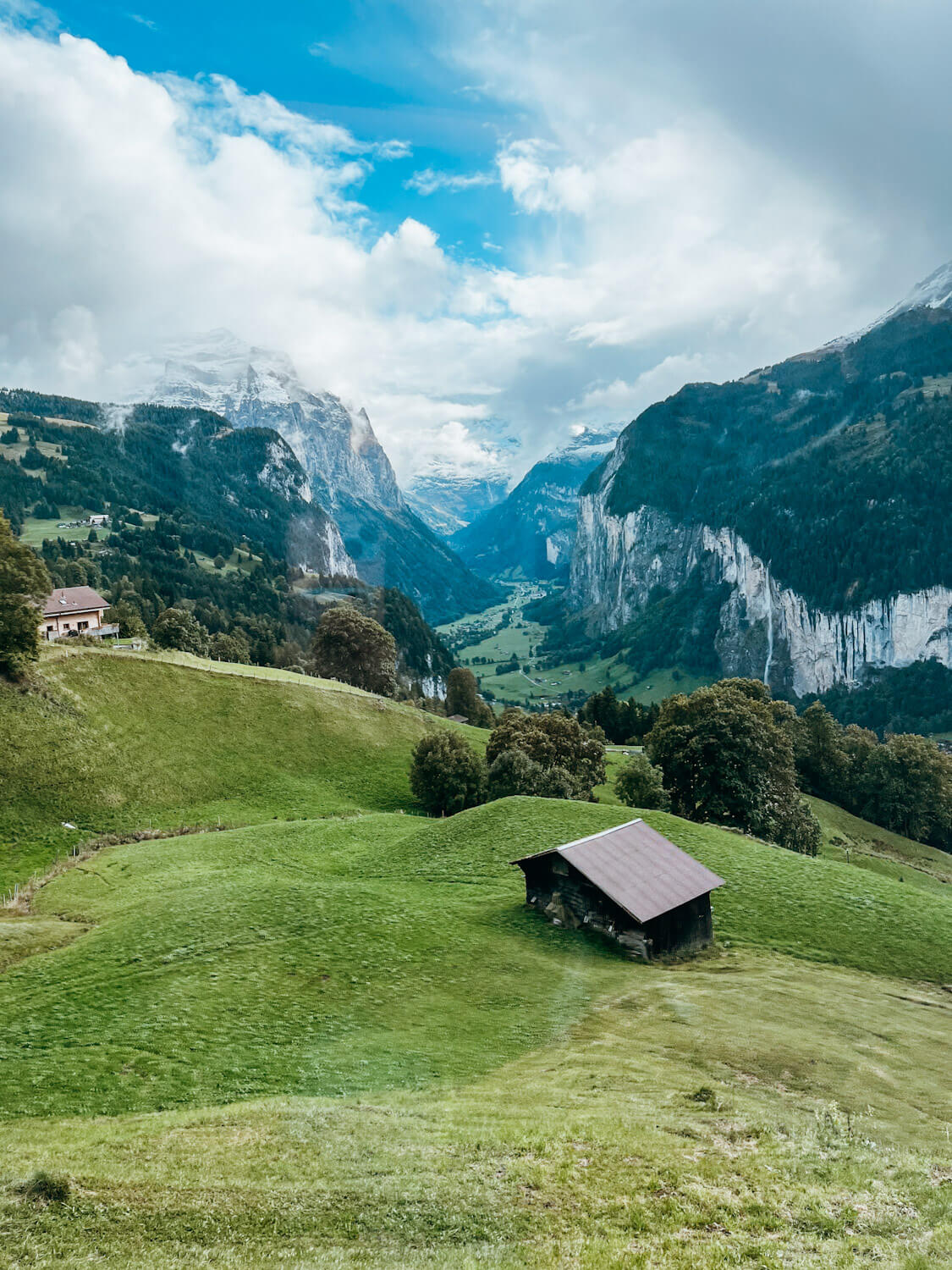 Wooden hut on rolling green hill with large mountains and valley in the background