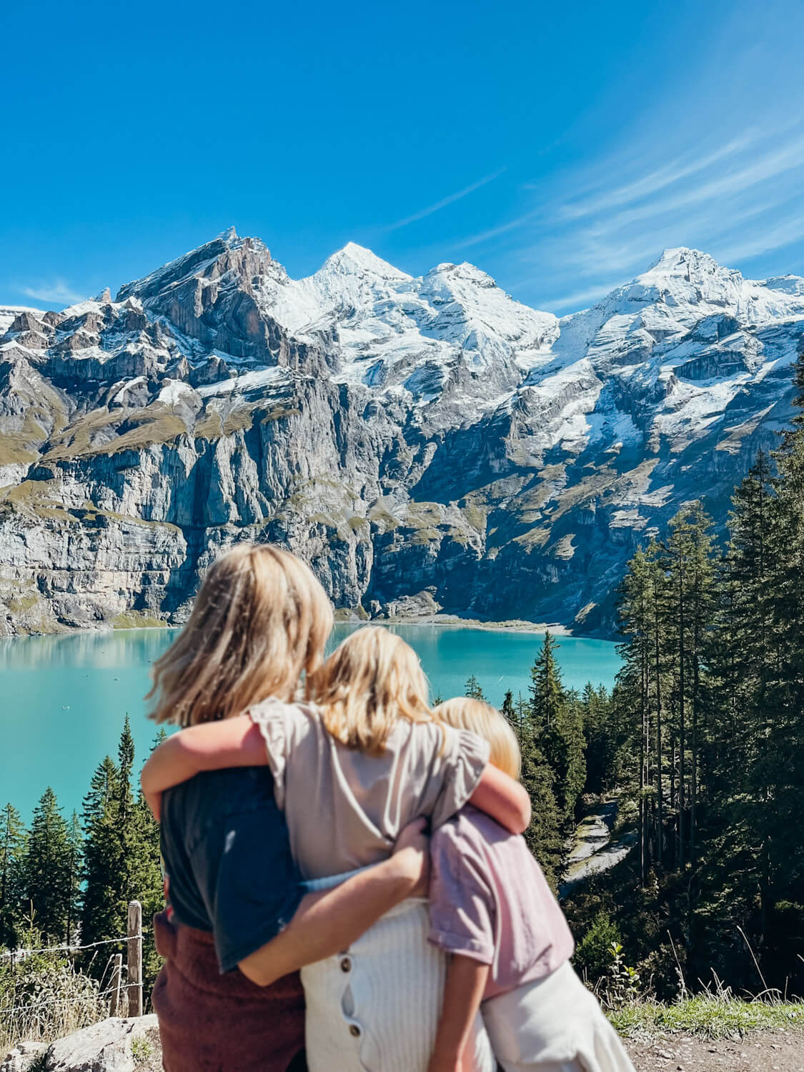 View from behind of mom and two kids hugging each other with view of blue mountain lake 