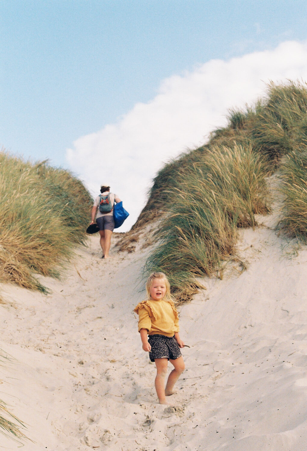 Man and child walk up large sandy hill with long green grass growing on each side heading to Vejers Strand Campgroun