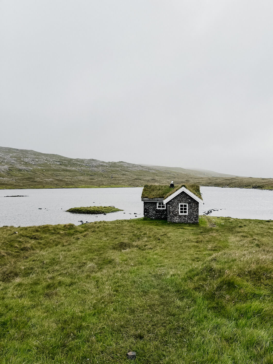 Stone cottage covered in grass next to pond on Sandoy Faroe Islands
