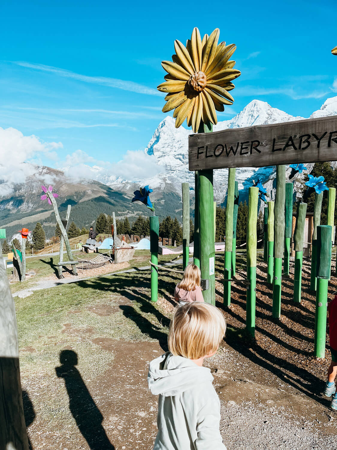 Wooden play structures at Allmendhubel Flower Park playground in Murren Switzerland with views of snow-capped mountain peaks
