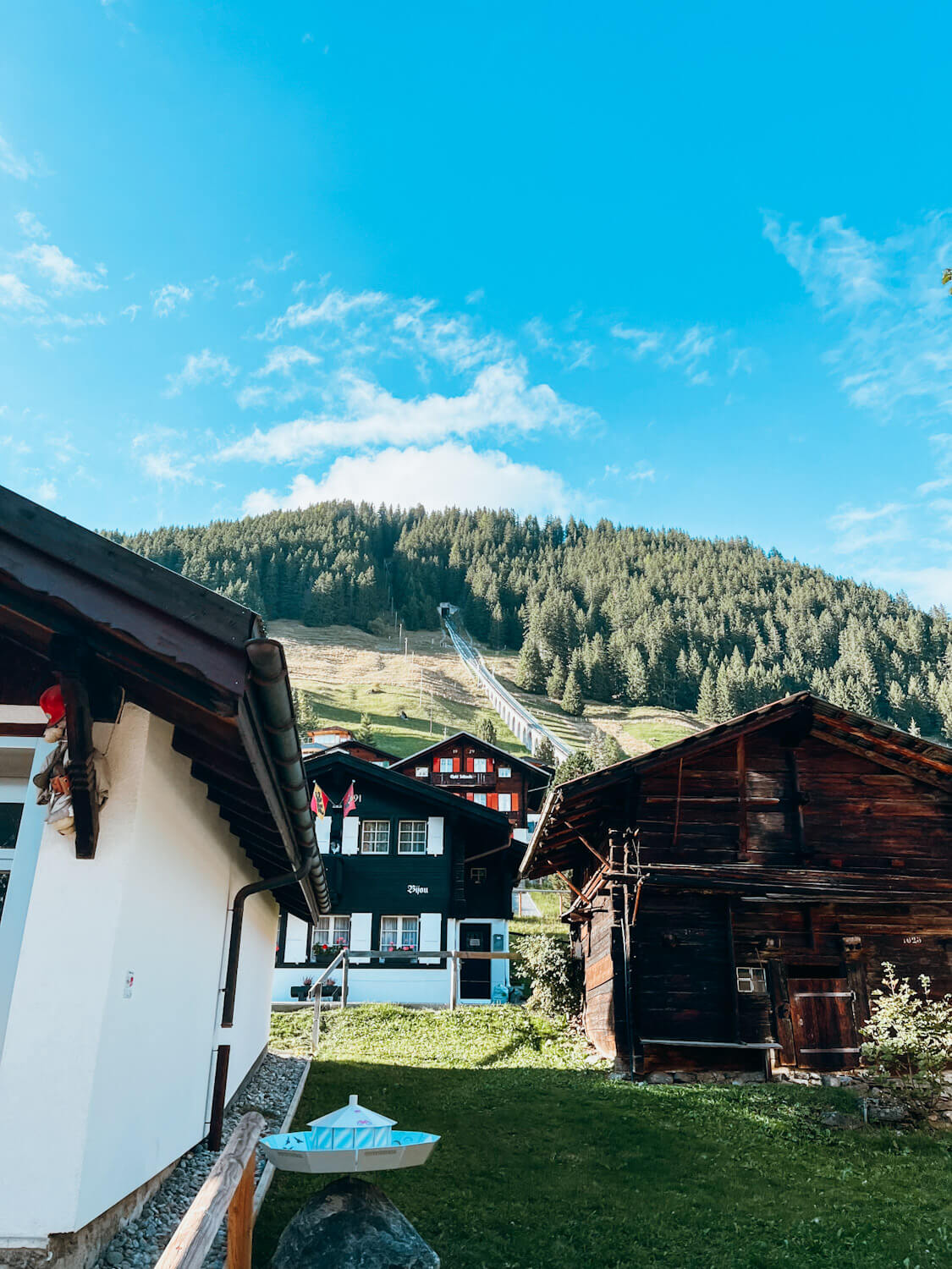 Wooden Swiss chalets in front of large grassy hill with a funicular track going up the side in Murren Switzerland