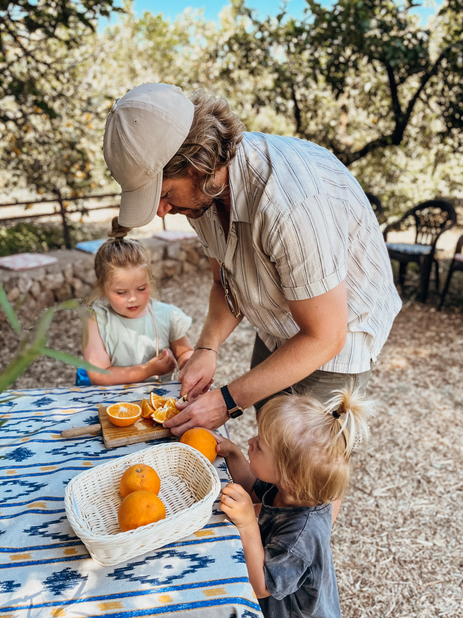 A father slices oranges for two kids at a table in the shade at Ecovinyassa