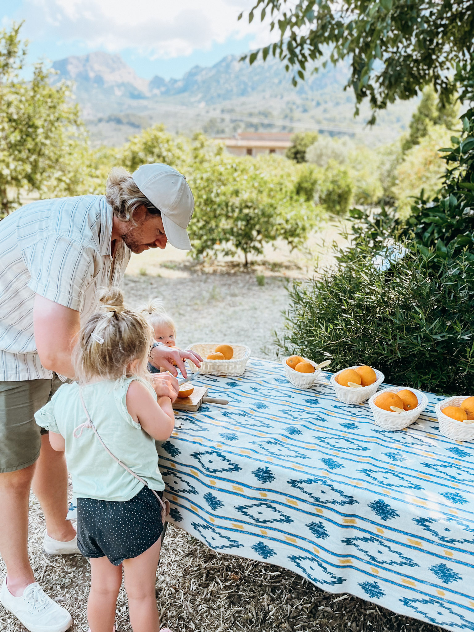 A father slices oranges for two kids at a table in the shade at Ecovinyassa