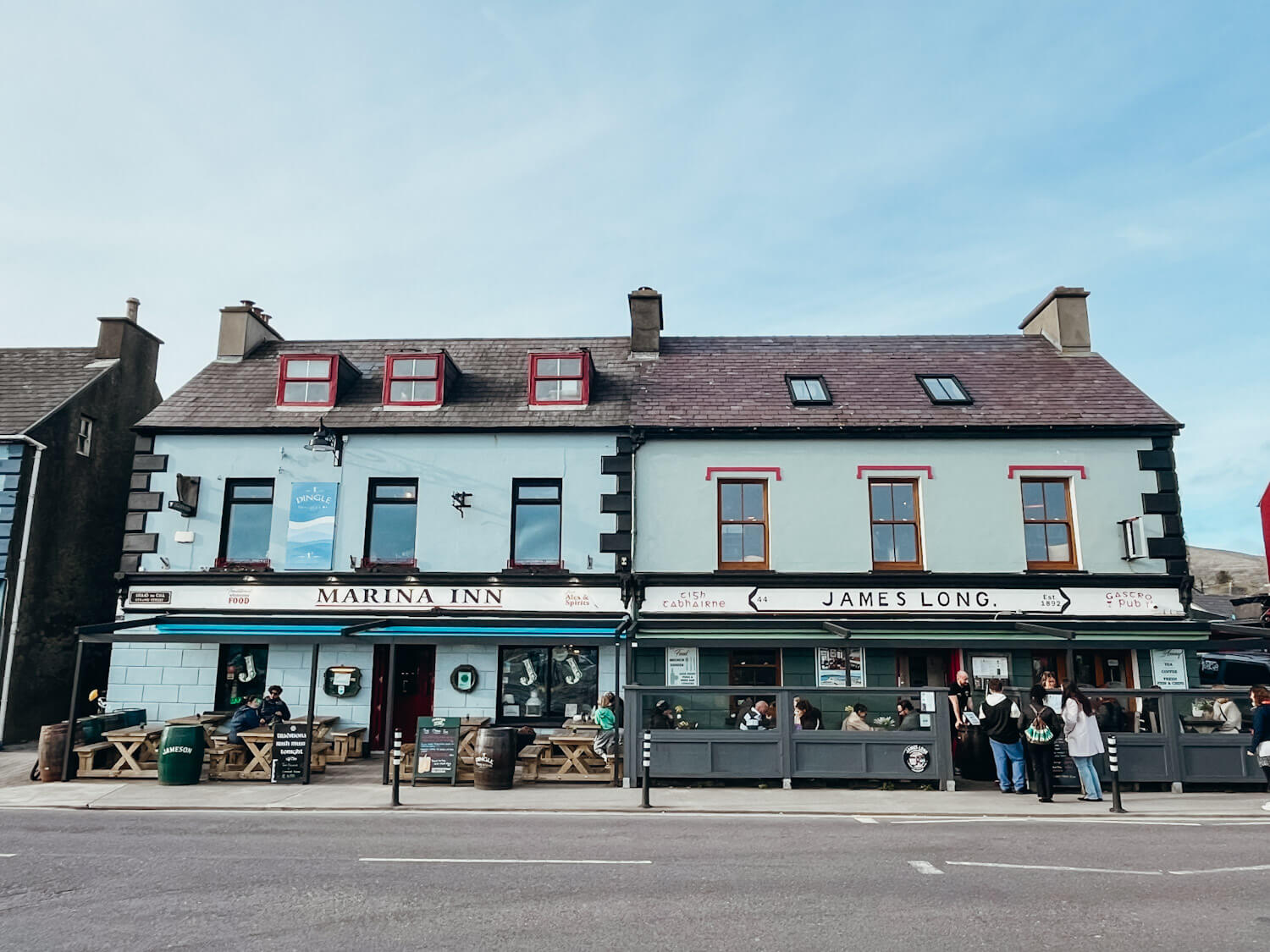 Blue and green older buildings housing pubs in Dingle Ireland with signs that read Marina Inn & James Long
