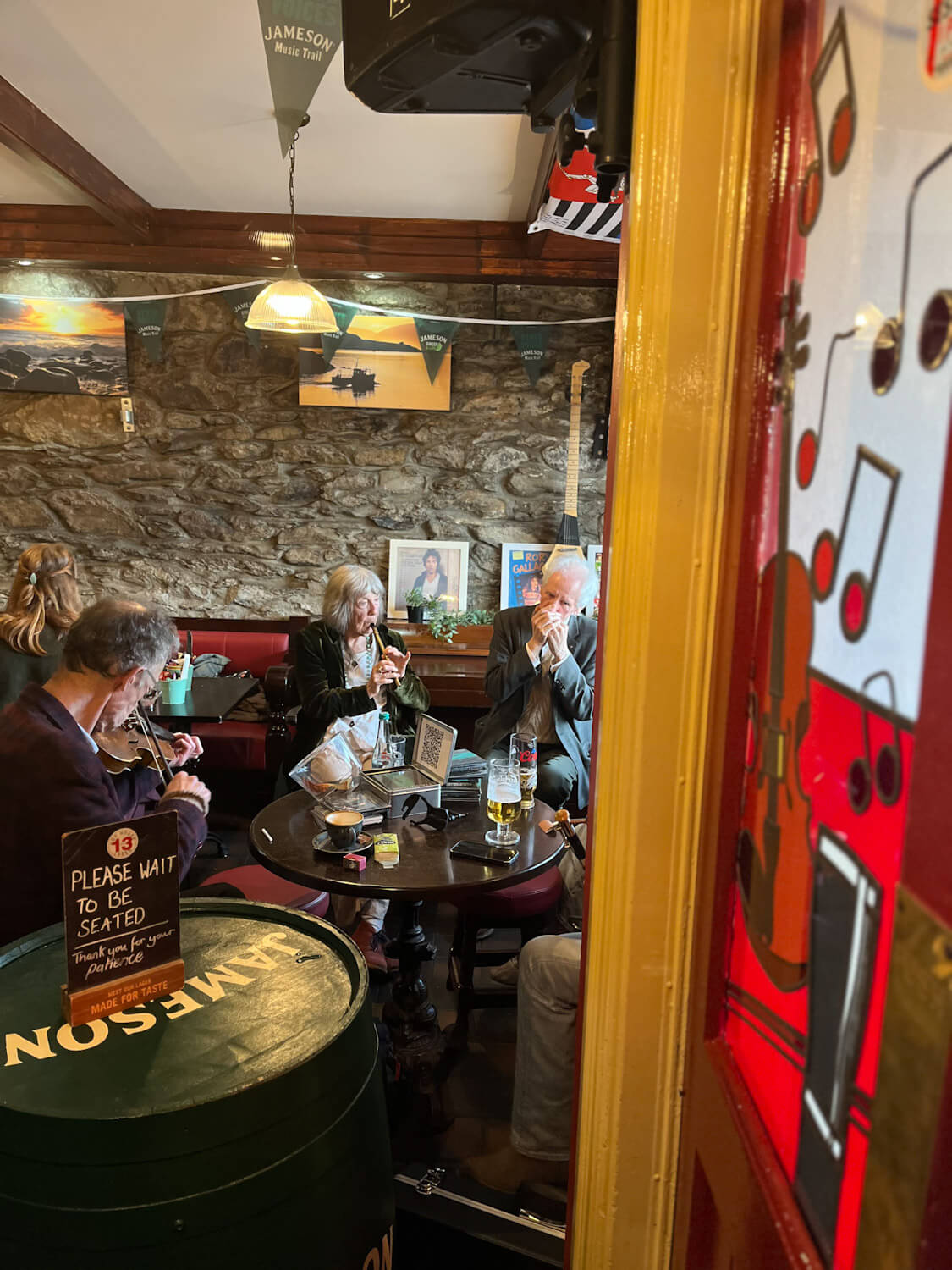 Three older people sit at round wooden table at pub in Dingle Ireland playing music