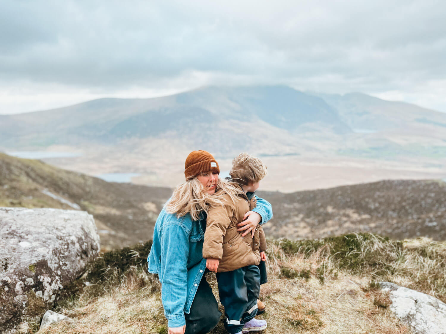 Woman and child stand on a hill with views of lakes and mountains behind