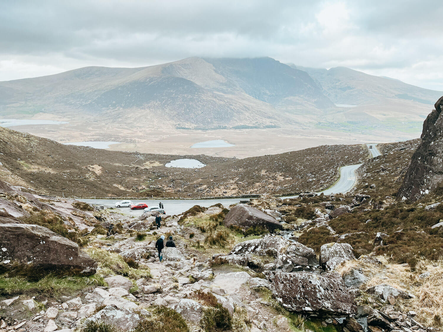 Panoramic view of rocks, lakes and mountains and a small car park on Connor Pass Dingle